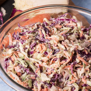 Bowl of vegan coleslaw, cutting board with cabbage, carrot and chef's knife in background