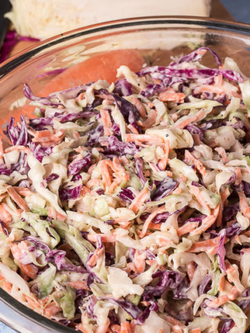 Bowl of vegan coleslaw, cutting board with cabbage, carrot and chef's knife in background