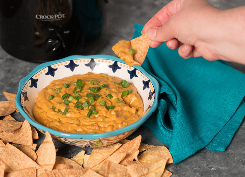 Dipping a chip in a bowl of Vegan Loaded Queso