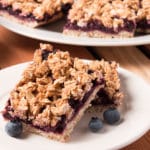 Plate with two Blueberry Oat Bars and some fresh blueberries. More bars in the background.