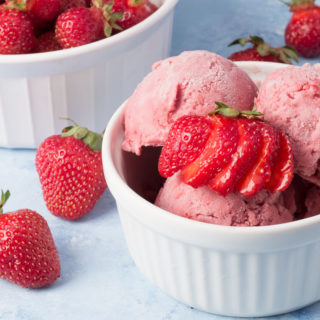 Bowl of vegan strawberry ice cream and bowl of strawberries in background