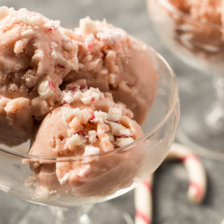 Two glass dessert dishes with Vegan Peppermint Ice Cream, with two candy canes sitting next to them