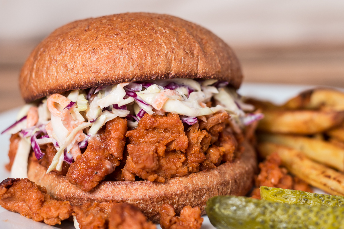 Closeup of BBQ Soy Curl Sandwich with pickles and baked fries on the side