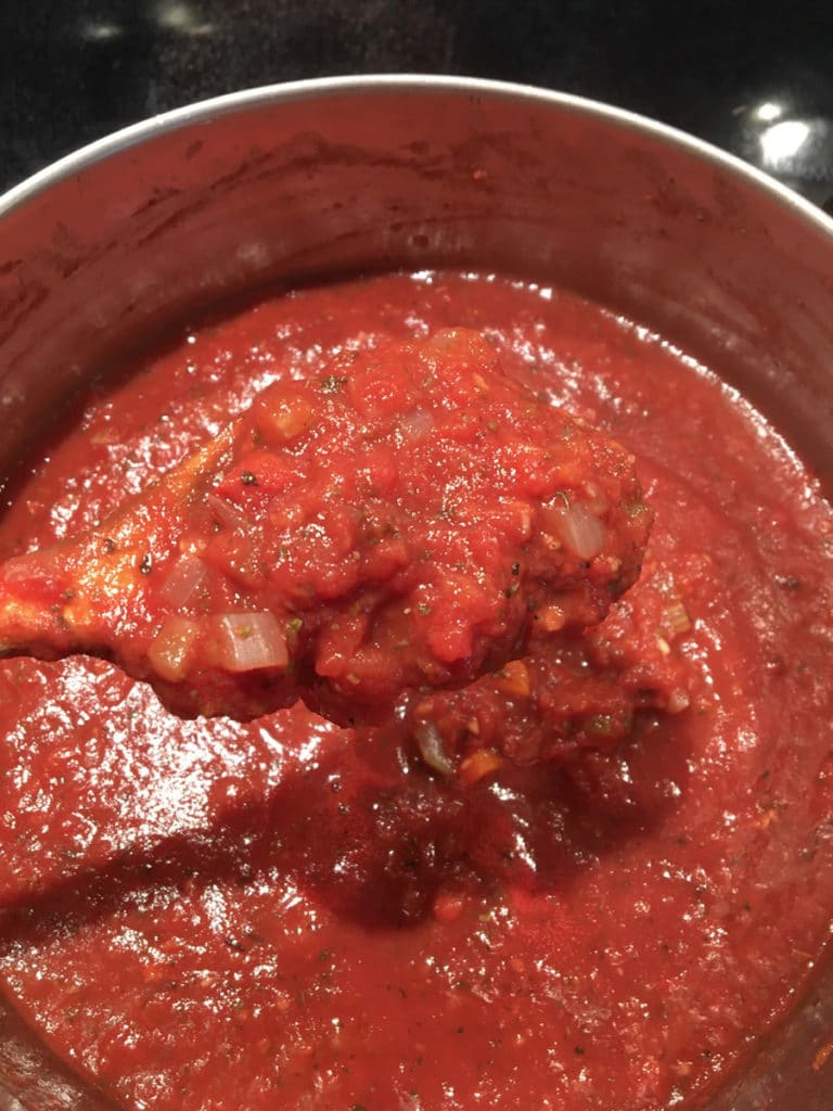 Pot of cooked marinara sauce with wooden spoon full of sauce