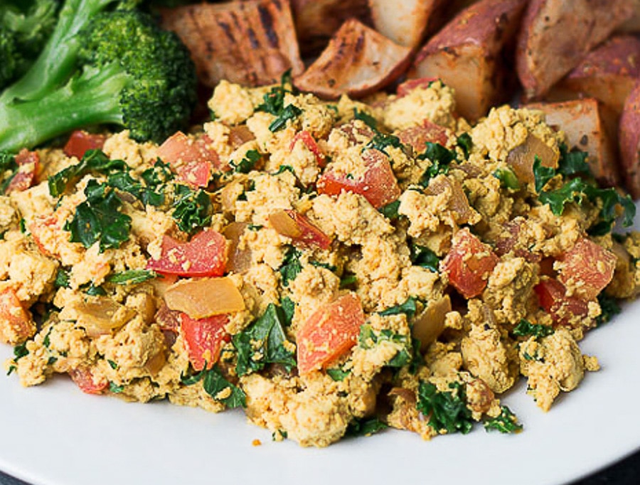 Closeup view of tofu scramble with kale and diced tomatoes; broccoli and roasted potatoes in background
