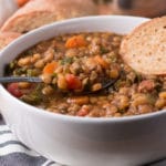 Bowl of lentil soup with spoon of soup and slice of bread in the bowl, more bread in background
