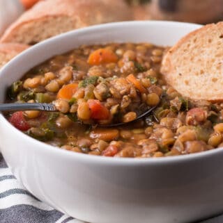 Bowl of lentil soup with spoon of soup and slice of bread in the bowl, more bread in background