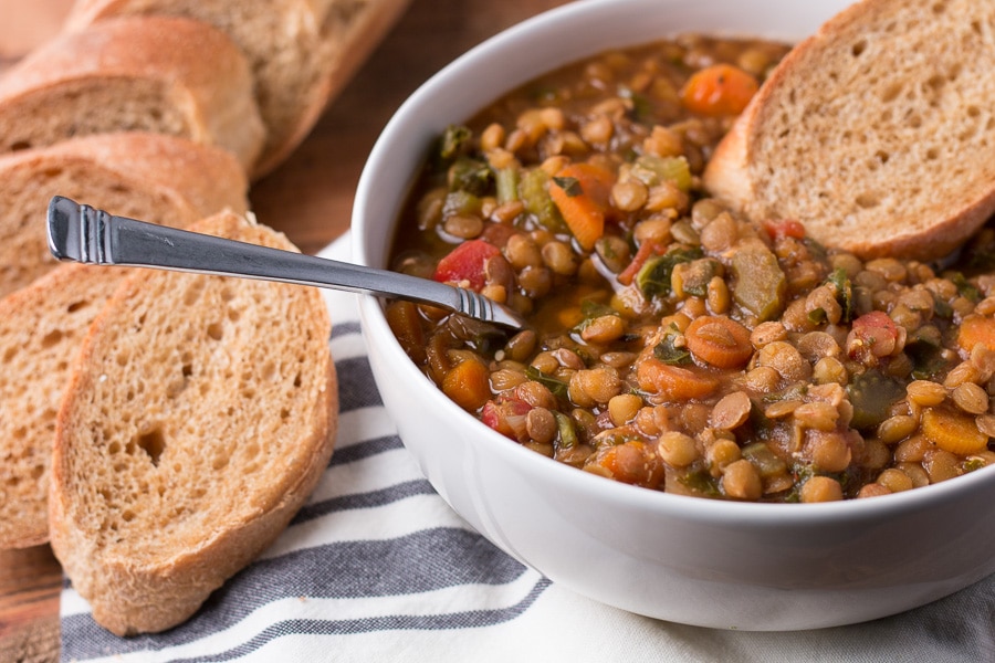 Bowl of lentil soup with spoon of soup and slice of bread in the bowl, more bread beside the bowl