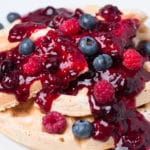 Plate of waffles topped with berry sauce, fresh blueberries, and fresh raspberries