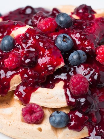 Plate of waffles topped with berry sauce, fresh blueberries, and fresh raspberries