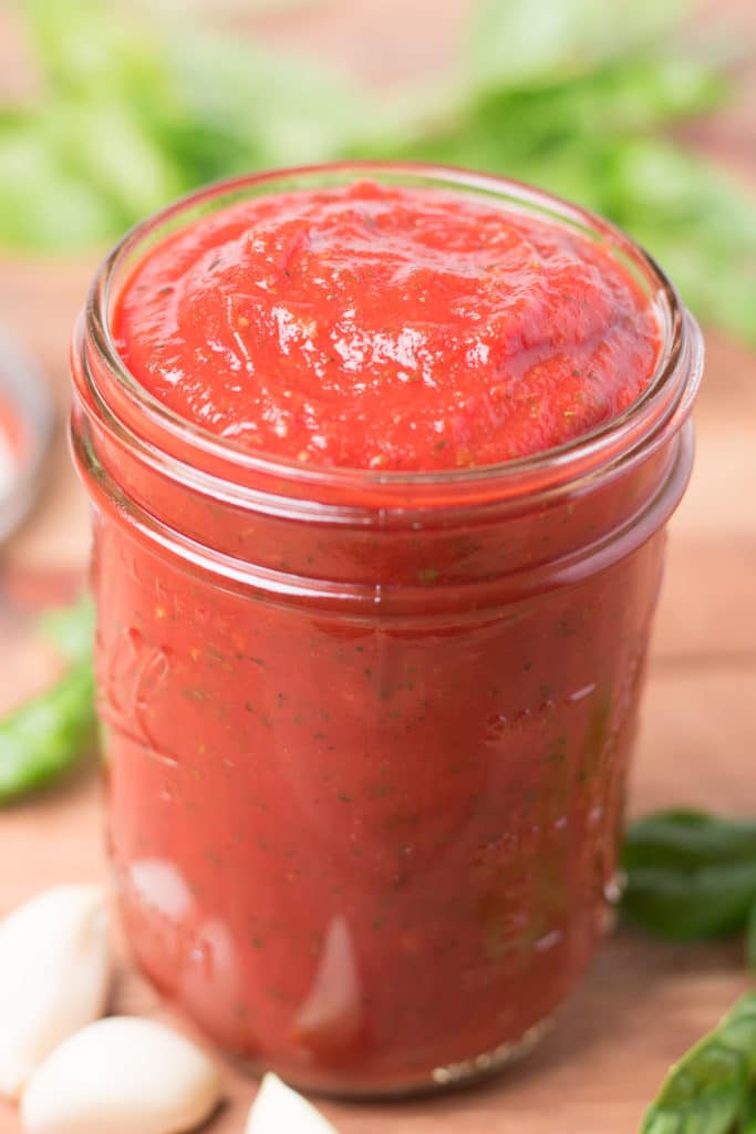 Jar of pizza sauce with fresh basil and garlic cloves around it