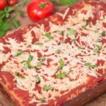 Pan of lasagna with tomatoes and basil in background