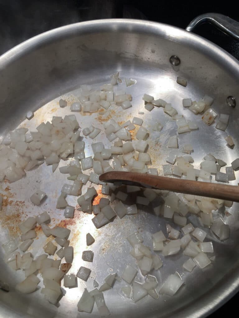 Onions cooking in stainless steel pan, with browned bits on surface of pan and wooden spoon