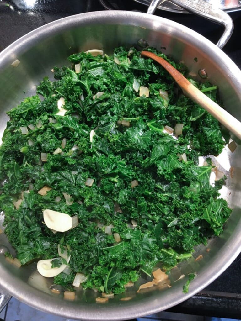 Cooked kale in stainless steel pan with wooden spoon