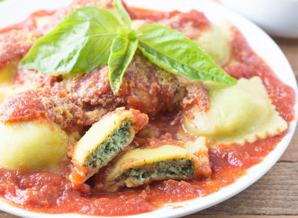 Plate of ravioli with tomato sauce topped with basil leaves; one ravioli cut in half