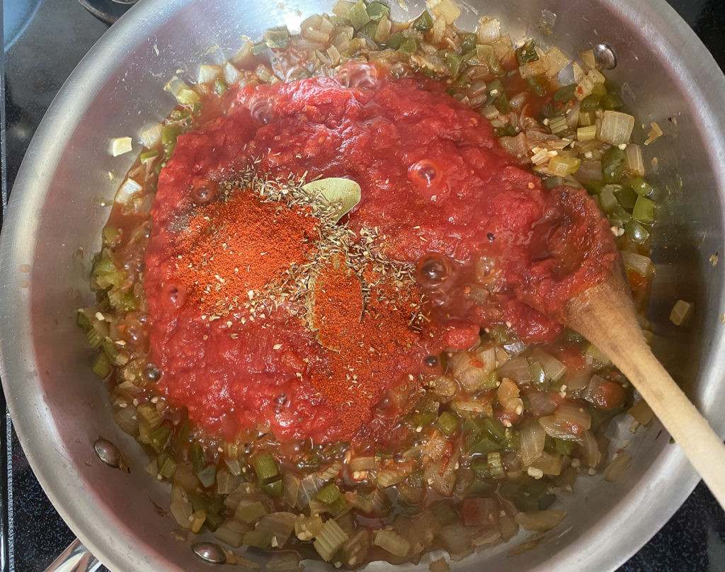 Tomatoes and spices added to pan of onions and peppers