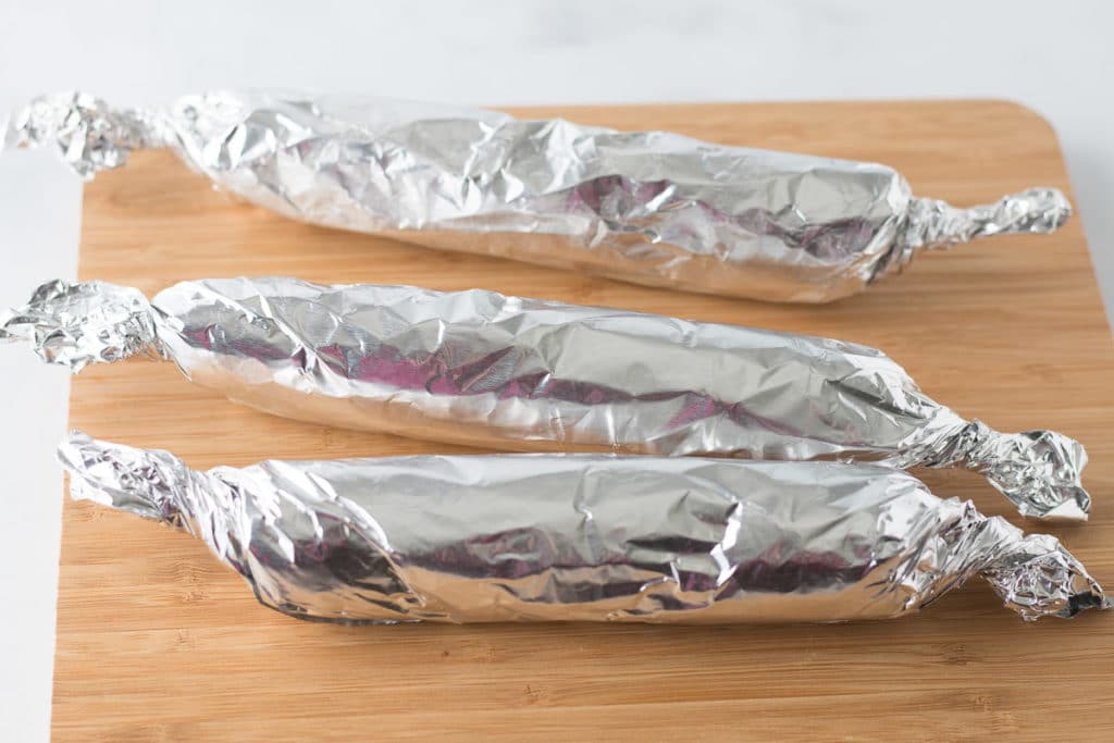 Three vegan sausages wrapped in foil on wooden cutting board