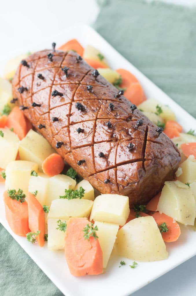 Vegan ham roast on platter with potatoes and carrots