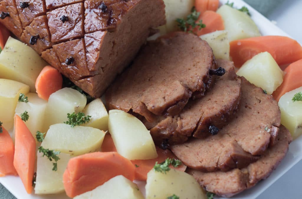 Closeup view of sliced vegan ham on platter with potatoes and carrots