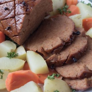 Closeup image of slilced vegan ham on platter with potatoes and carrots