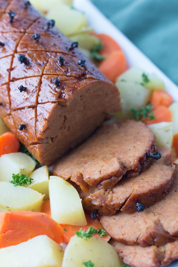 Sliced vegan ham on platter with potatoes and carrots