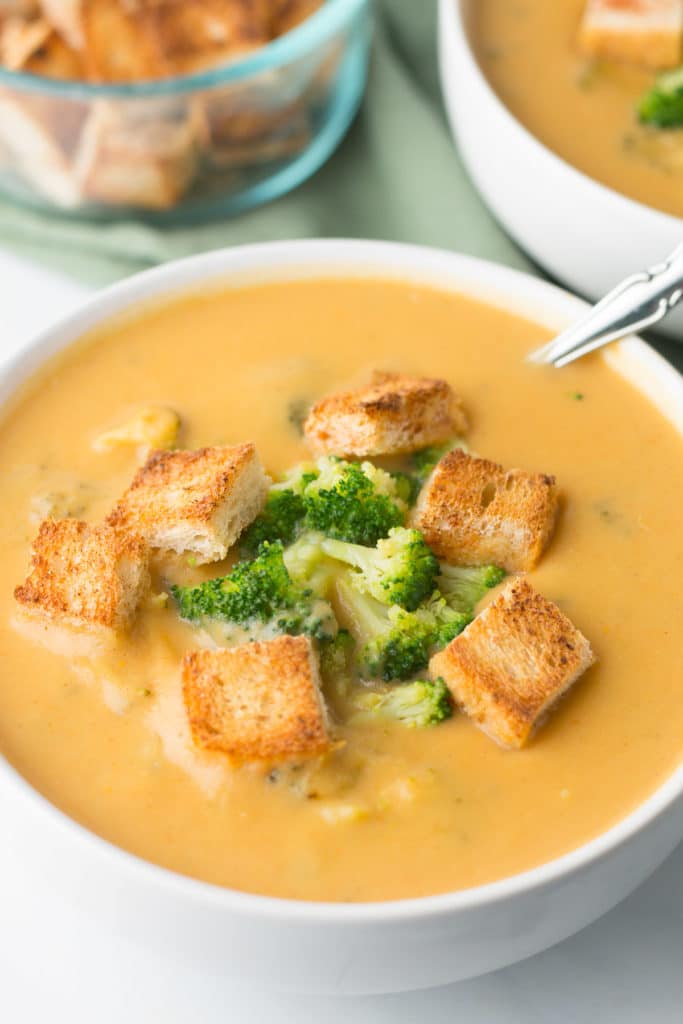 Bowl of Broccoli Cheddar Soup with another bowl of soup and bowl of croutons in background