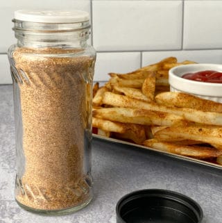 Jar of seasoning with plate of fries in background