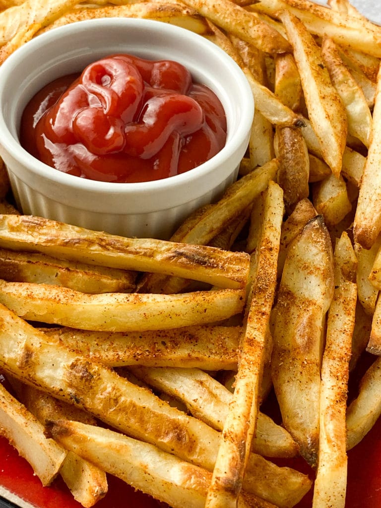 Plate of seasoned french fries with cup of ketchup