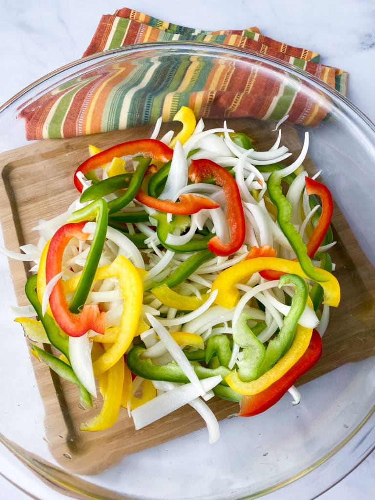 Sliced onions and bell peppers in a glass bowl