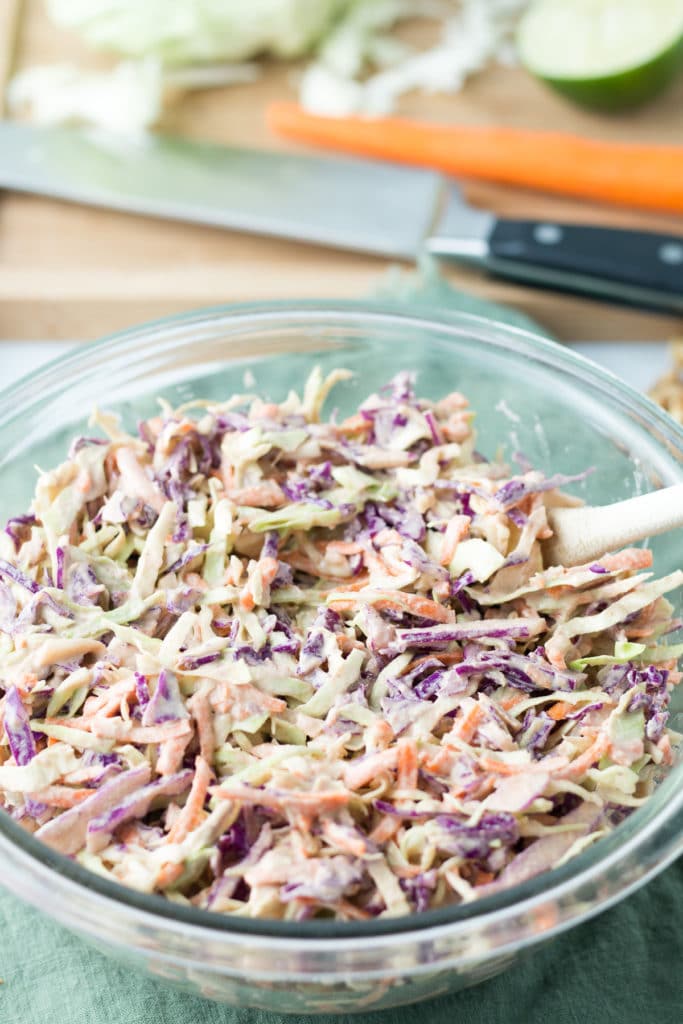 Bowl of coleslaw in front of cutting board with knife and vegetables