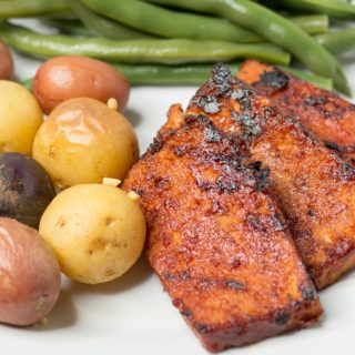 White plate with bbq tofu slices, baby potatoes, and green beans