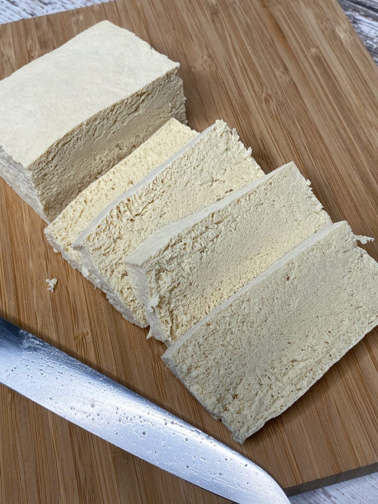 Slices of tofu and a knife on a wooden cutting board