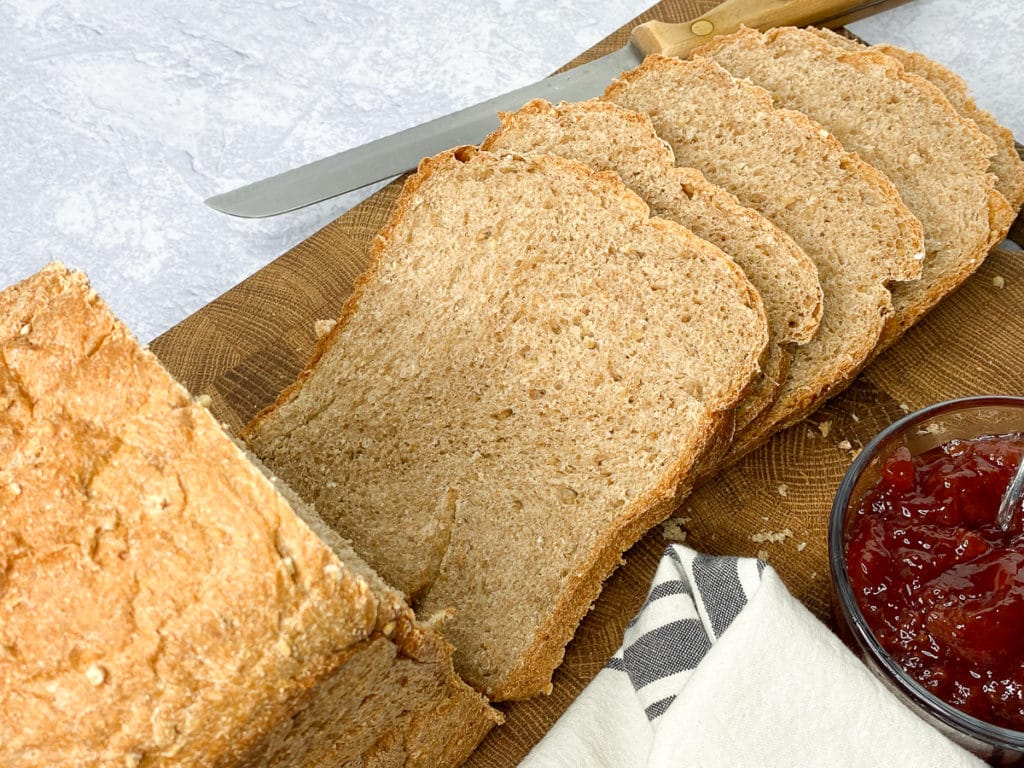Loaf of bread sliced on a cutting board with knife and bowl of jam next to it