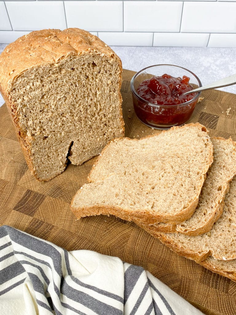 Loaf of bread sliced on a cutting board with knife and bowl of jam next to it