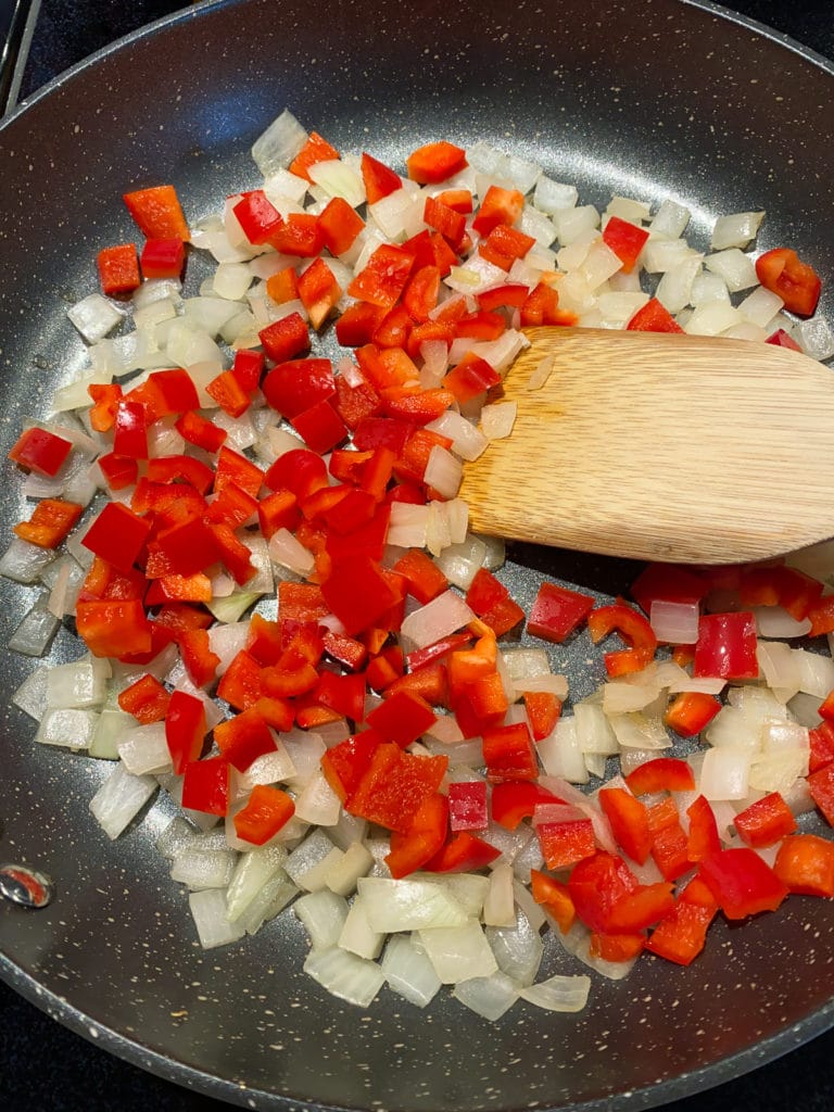Diced red bell peppers added to skillet of diced onions