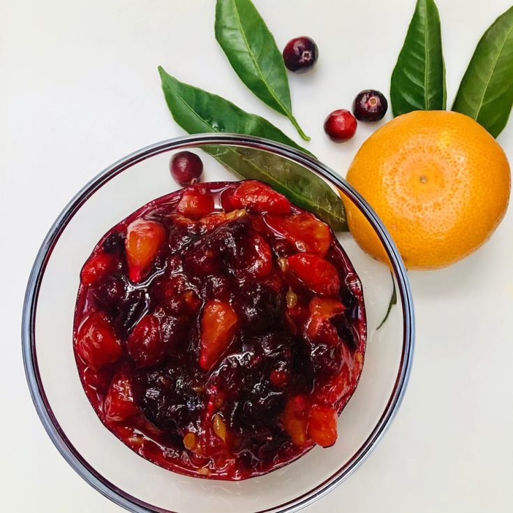 Dish of cranberry orange sauce with small orange and fresh canberries beside it