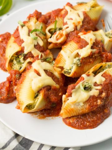 Plate of stuffed shells on a striped napkin with fresh basil and tomato in background