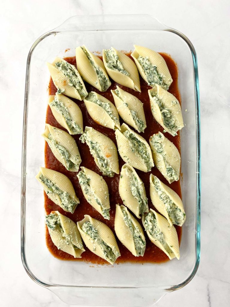 Unbaked stuffed shells on layer of marinara in a glass baking pan
