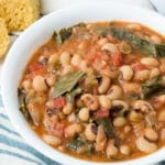 Bowl of black eyed peas on a striped napkin with pieces of corbread next to it