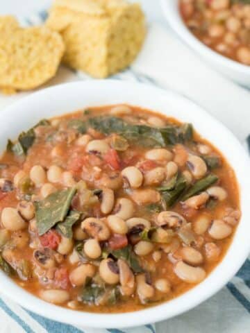Bowl of black eyed peas and greens with another bowl and cornbread in background