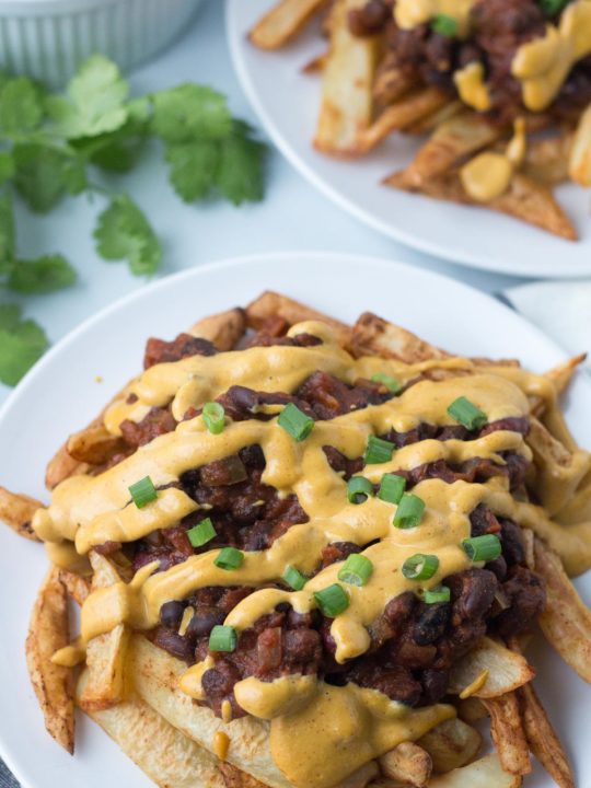Plate of vegan chili cheese fries with another plate of chili cheese fries in background