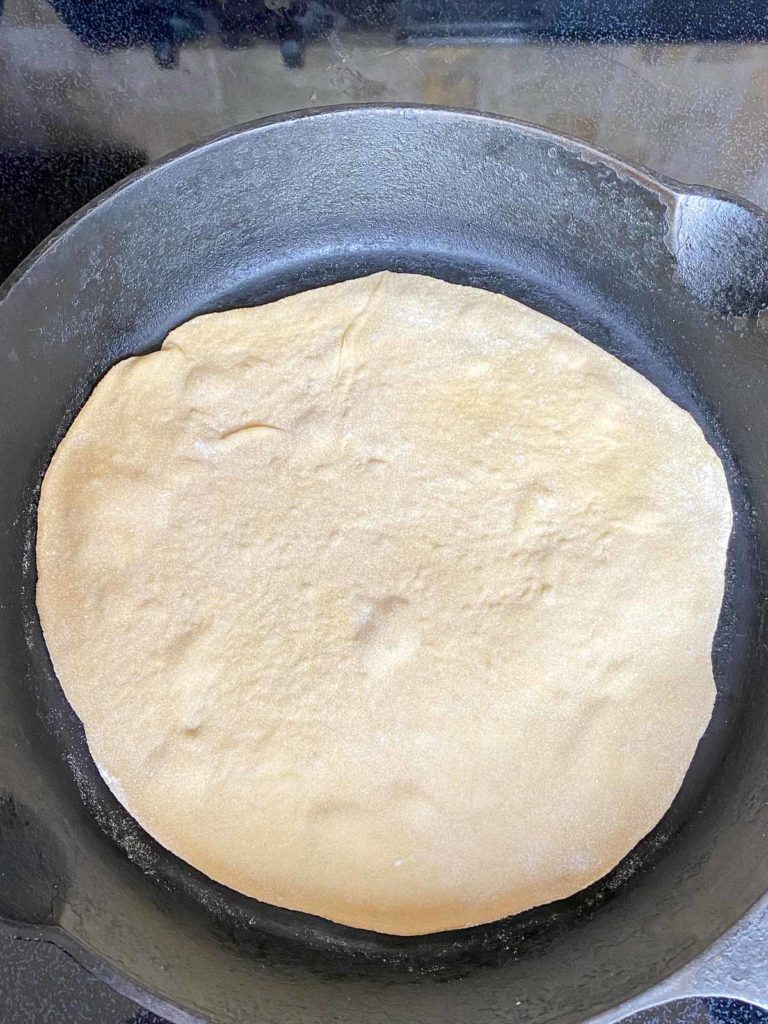 First side of tortilla cooking in a cast iron skillet