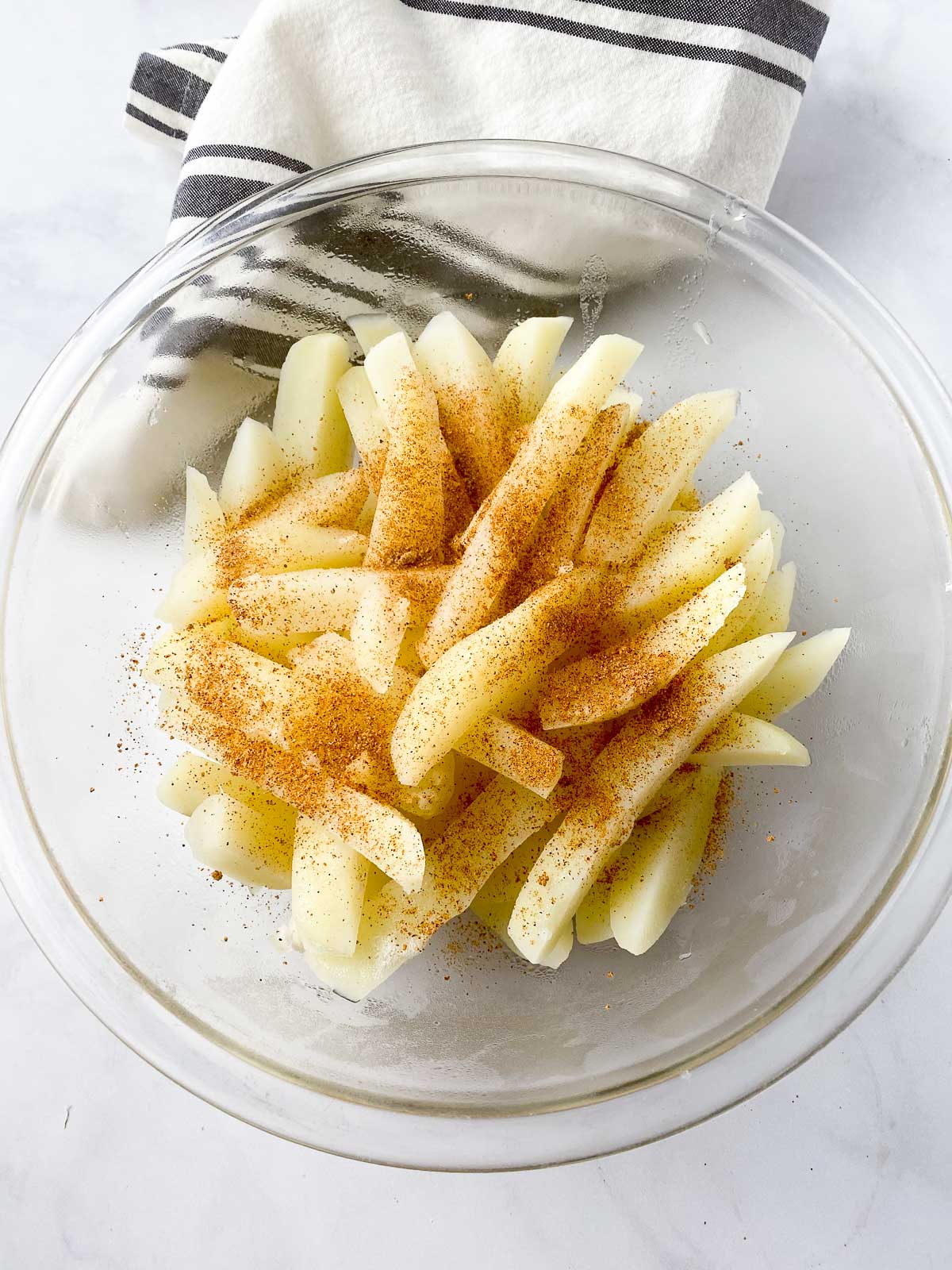 Sliced potatoes and seasoning in glass mixing bowl
