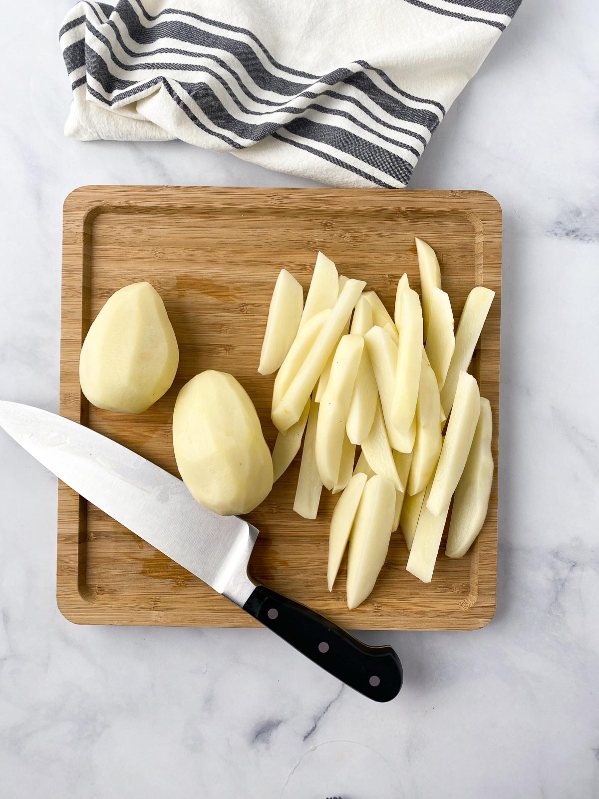 Peeled and fry cut potatoes on a cutting board.