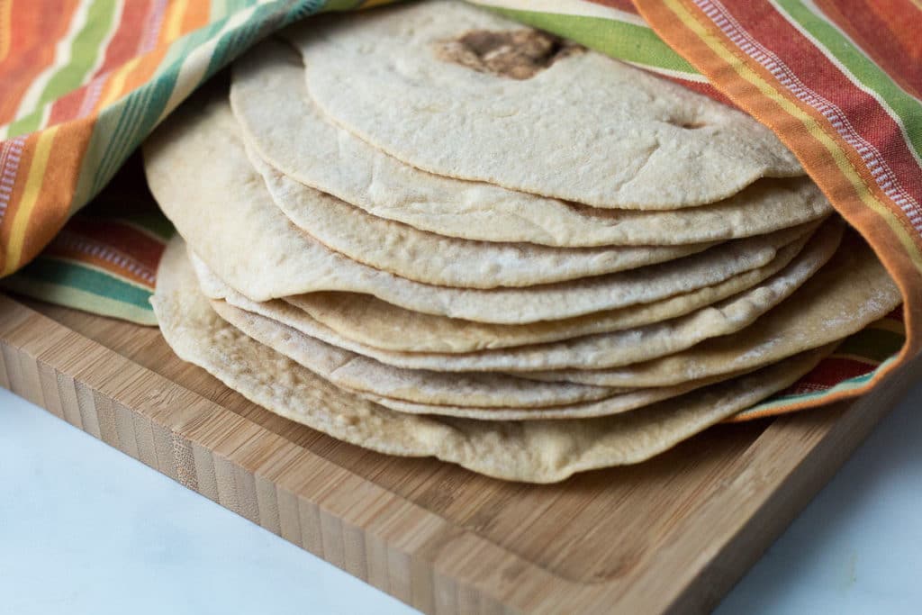Closeup image of whole wheat tortillas on a cutting board covered with stritped towel