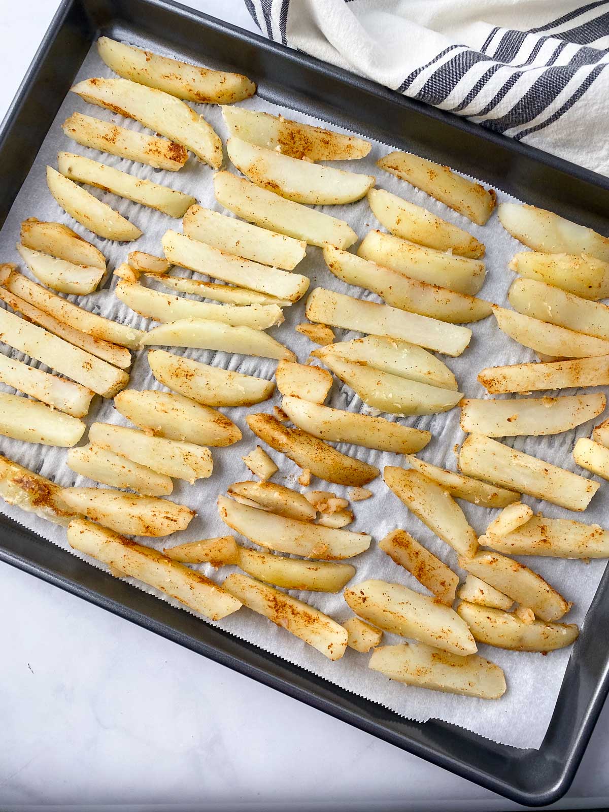 Unbaked fries on parchment lined baking sheet