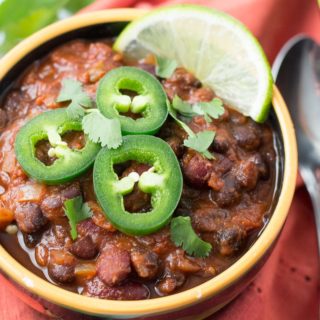 Bowl of chili garnished with jalapeno slices, cilantro, and lime slice
