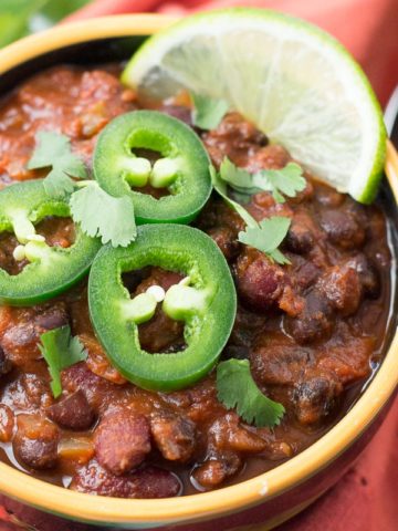 Bowl of chili garnished with jalapeno slices, cilantro, and lime slice