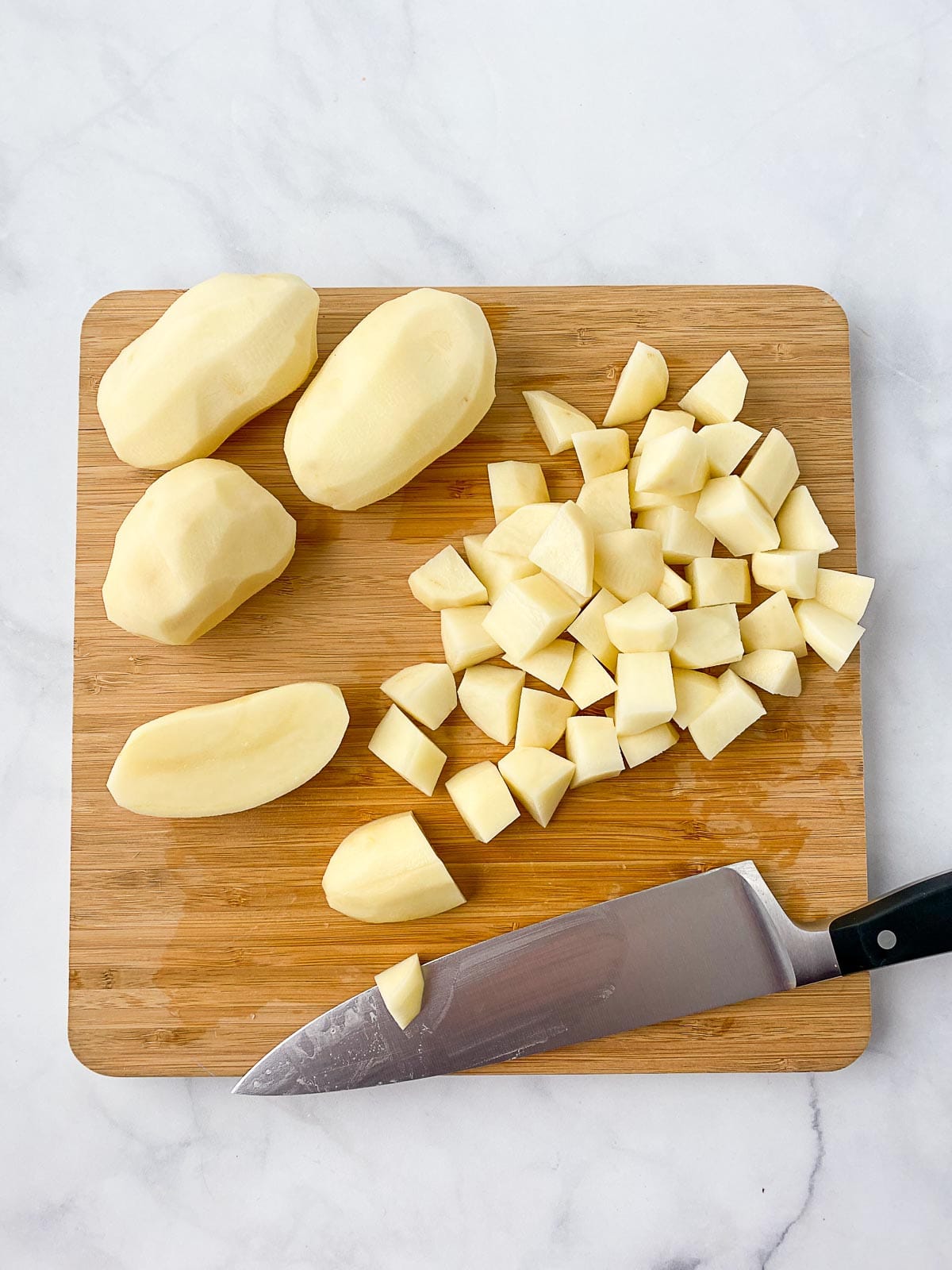 Whole and diced potatoes on a wooden cutting board.