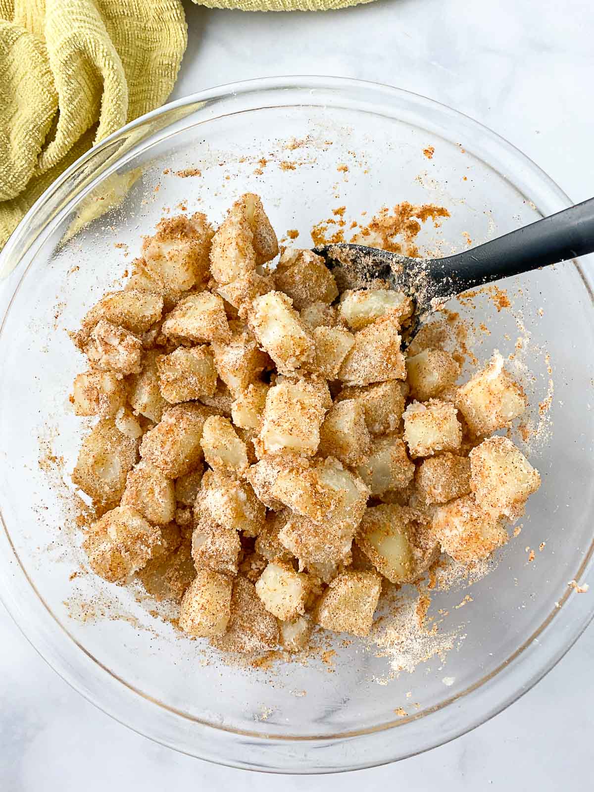 Diced potatoes coated with seasoning in a glass bowl.